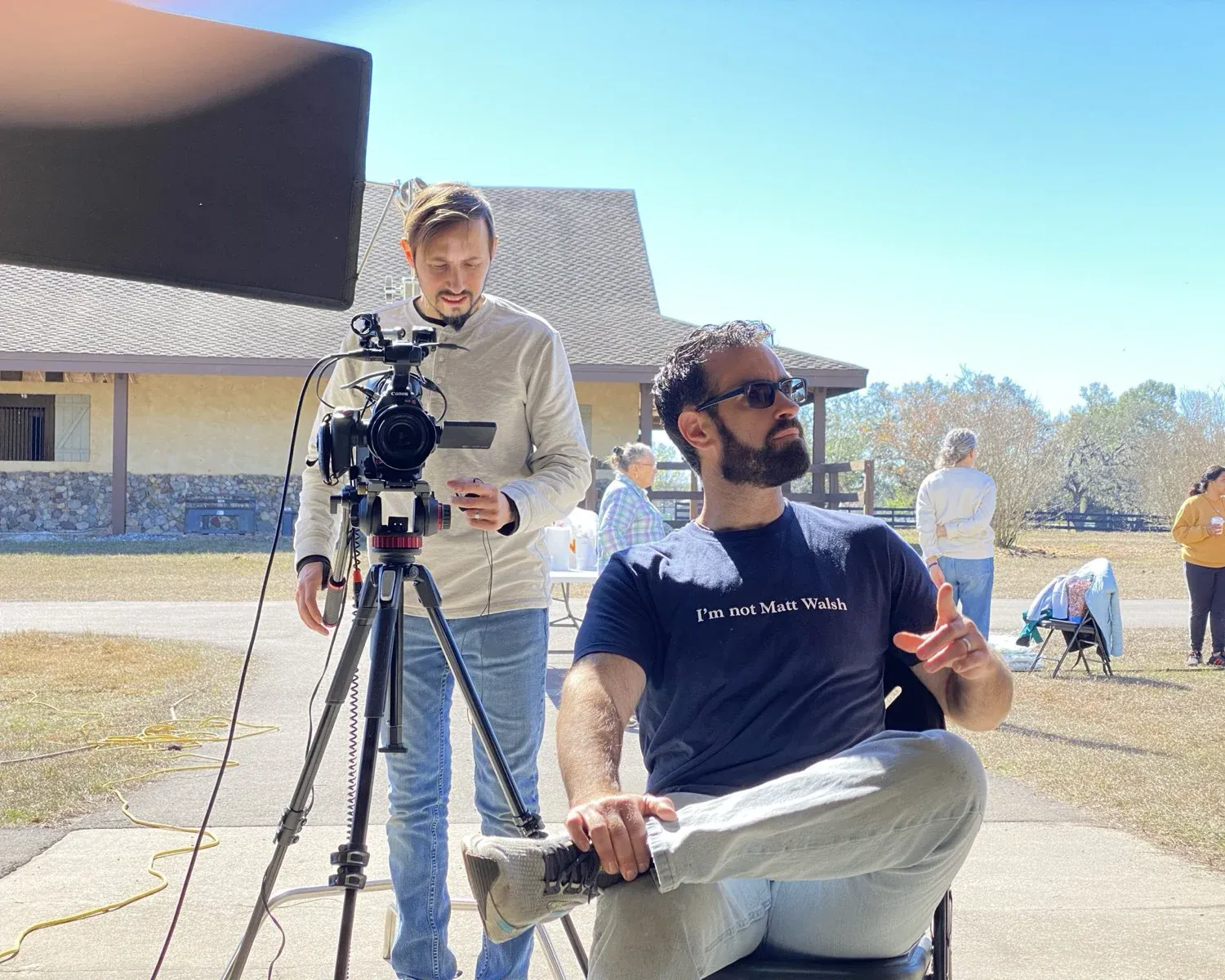 A production team films an interview outdoors beside a camera on a tripod.