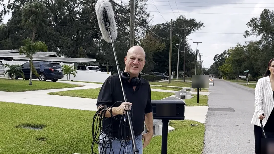 Crew member operating a boom microphone outdoors during production